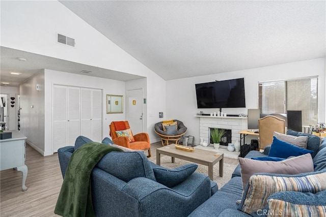 living room featuring a brick fireplace, high vaulted ceiling, and light hardwood / wood-style flooring