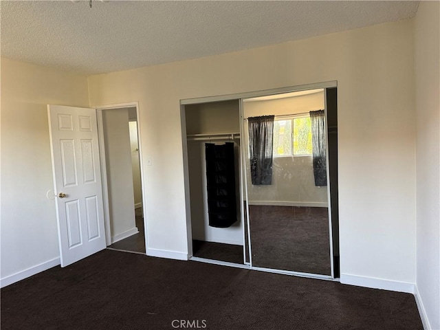 unfurnished bedroom with a closet, dark carpet, and a textured ceiling