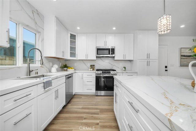 kitchen featuring appliances with stainless steel finishes, tasteful backsplash, sink, white cabinets, and hanging light fixtures