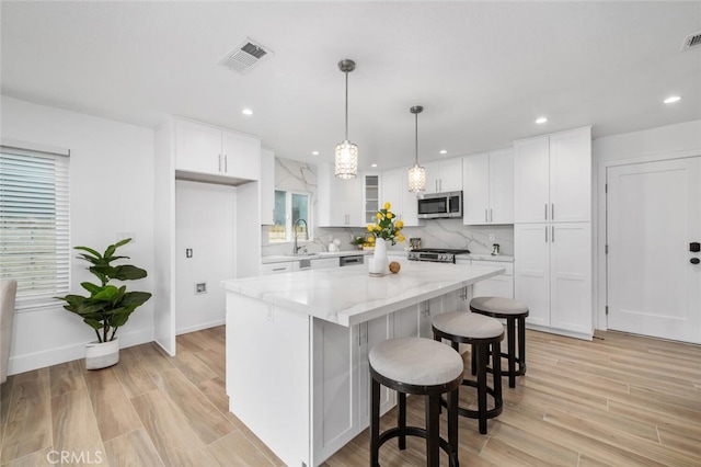 kitchen featuring sink, appliances with stainless steel finishes, a kitchen island, light stone counters, and white cabinetry