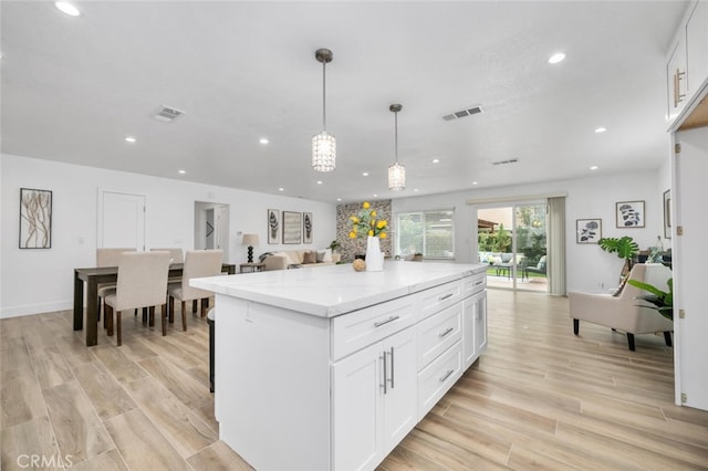 kitchen with pendant lighting, a center island, white cabinets, light hardwood / wood-style flooring, and light stone countertops