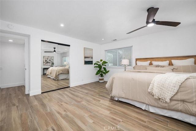 bedroom with a fireplace, light wood-type flooring, and ceiling fan