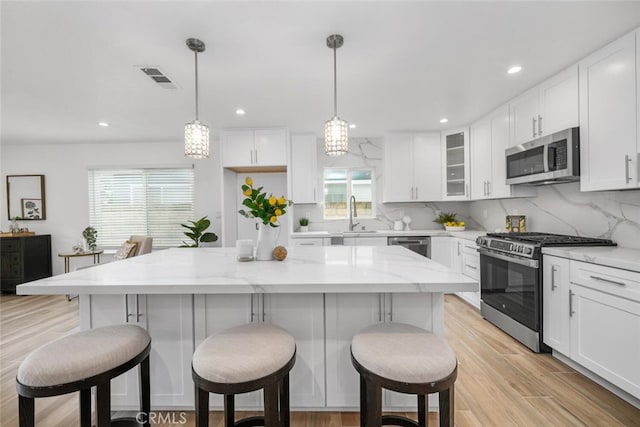 kitchen with light stone countertops, a center island, decorative light fixtures, white cabinets, and appliances with stainless steel finishes