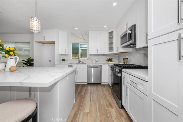 kitchen with light stone countertops, stainless steel appliances, decorative light fixtures, a kitchen bar, and white cabinets