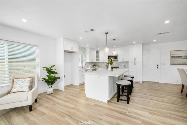 kitchen featuring sink, decorative light fixtures, a center island, light hardwood / wood-style floors, and white cabinetry