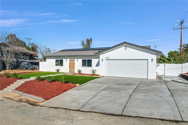 single story home featuring solar panels, concrete driveway, stucco siding, fence, and a front yard