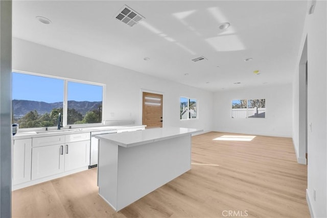 kitchen featuring sink, a mountain view, a center island, light hardwood / wood-style floors, and white cabinetry