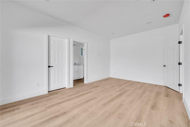 unfurnished bedroom featuring ensuite bath, light wood-style flooring, and baseboards