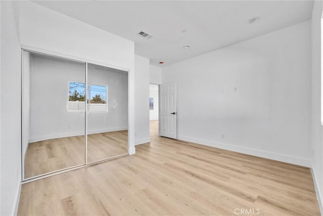 unfurnished bedroom featuring a closet, wood finished floors, visible vents, and baseboards