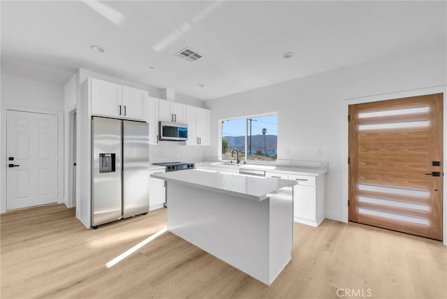 kitchen with a sink, a kitchen island, light wood-style floors, white cabinets, and appliances with stainless steel finishes