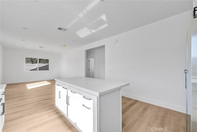 kitchen with light hardwood / wood-style flooring, white cabinetry, a kitchen island, and light stone counters