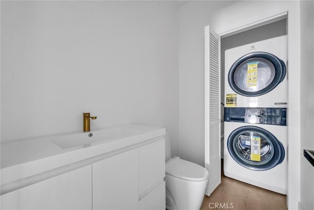 bathroom featuring hardwood / wood-style flooring, sink, stacked washer and clothes dryer, and toilet