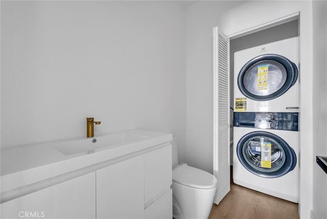 bathroom with stacked washer and clothes dryer, a sink, toilet, and wood finished floors