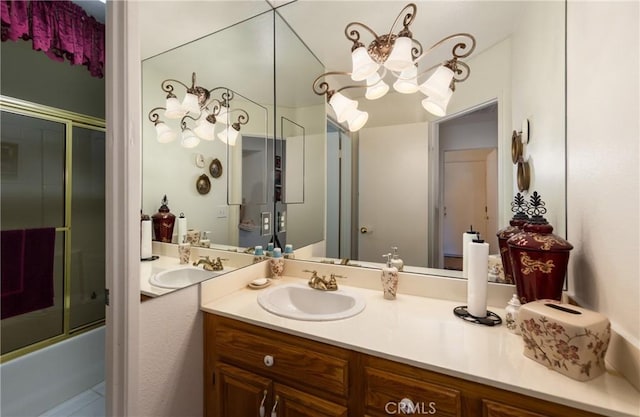 bathroom featuring a chandelier, combined bath / shower with glass door, and vanity