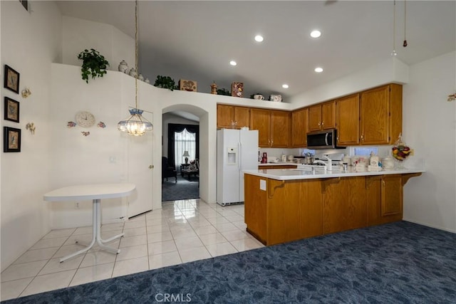 kitchen with brown cabinetry, a peninsula, arched walkways, white fridge with ice dispenser, and stainless steel microwave