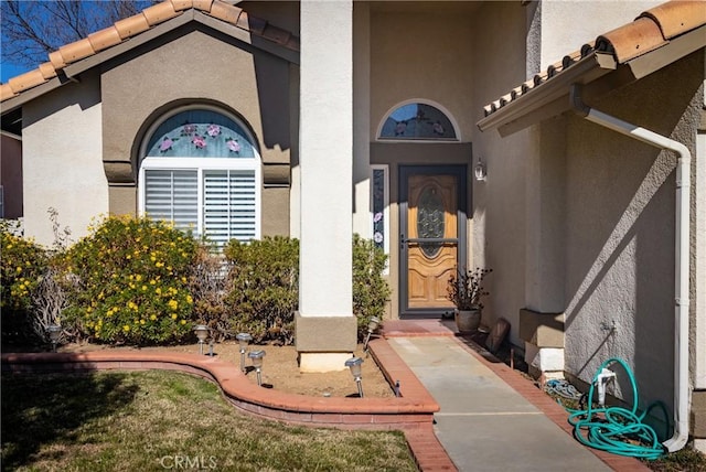 entrance to property featuring a tiled roof and stucco siding