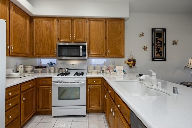 kitchen featuring brown cabinetry, stainless steel microwave, a sink, and white gas range oven