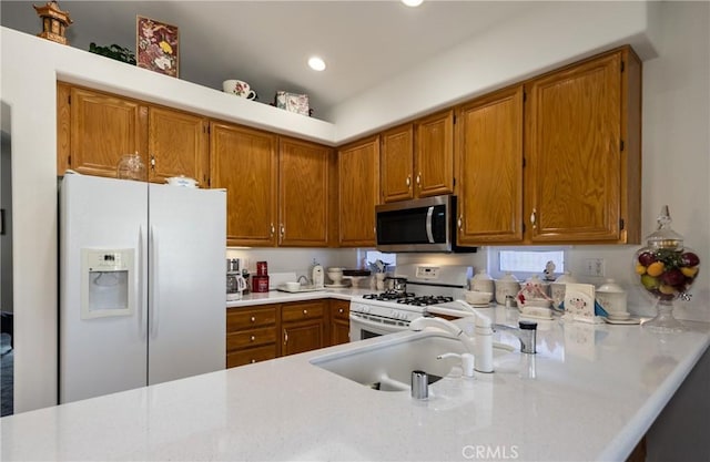 kitchen featuring a sink, white appliances, light countertops, and brown cabinetry
