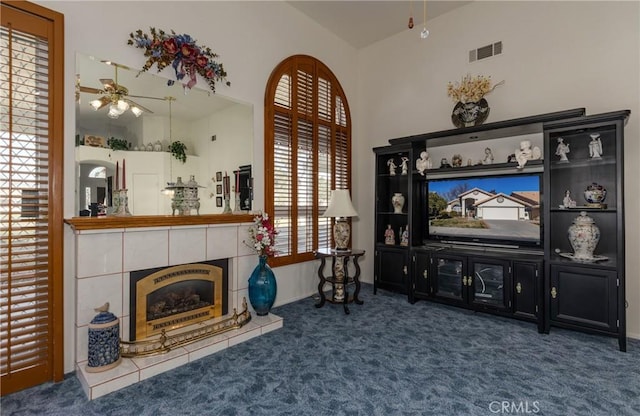 carpeted living room with a towering ceiling, a tile fireplace, visible vents, and ceiling fan