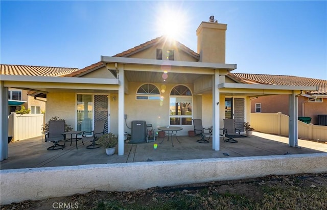 rear view of house with stucco siding, a chimney, a patio, and fence