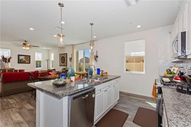 kitchen with appliances with stainless steel finishes, a kitchen island with sink, decorative light fixtures, white cabinets, and sink