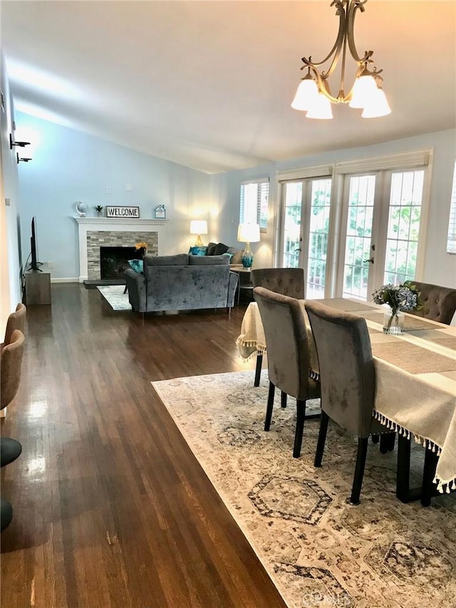 dining room featuring french doors, dark wood-type flooring, a notable chandelier, vaulted ceiling, and a fireplace