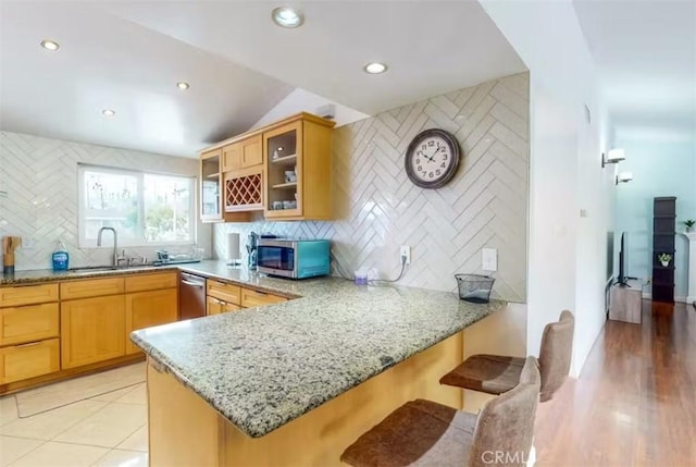 kitchen featuring a breakfast bar area, kitchen peninsula, light stone counters, and stainless steel appliances