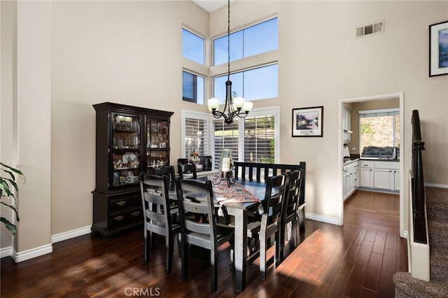 dining space with a towering ceiling, an inviting chandelier, a healthy amount of sunlight, and dark wood-type flooring