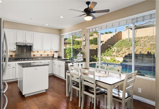 kitchen featuring stainless steel appliances, a kitchen island, dark hardwood / wood-style flooring, white cabinetry, and dark stone countertops