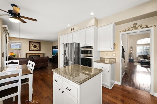 kitchen with dark stone countertops, appliances with stainless steel finishes, a tiled fireplace, dark hardwood / wood-style flooring, and white cabinets