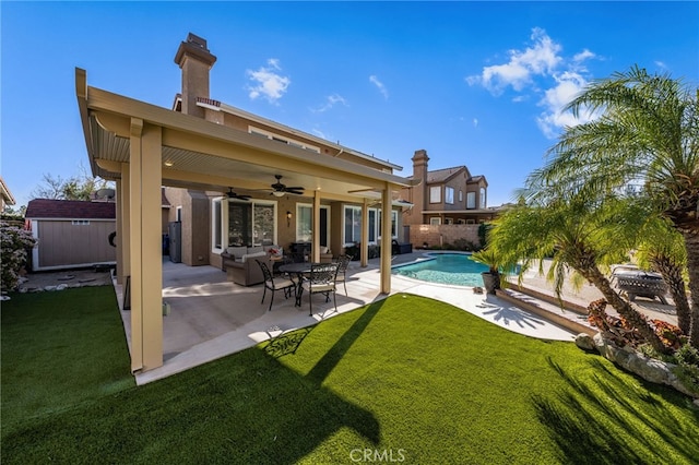 rear view of property with ceiling fan, a patio, a yard, and a storage shed