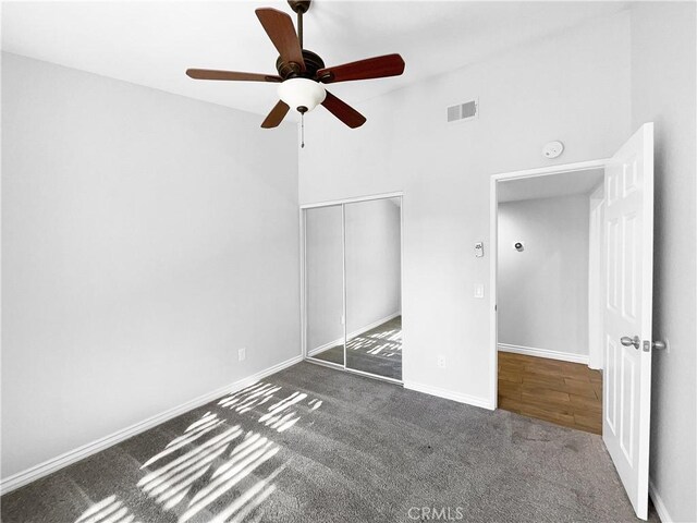 unfurnished bedroom featuring a high ceiling, ceiling fan, dark carpet, and a closet