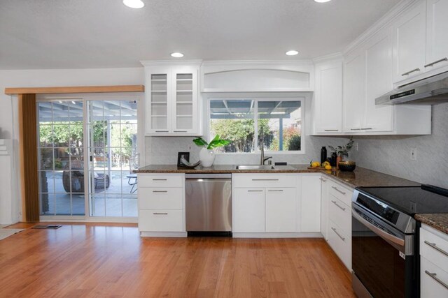 kitchen with appliances with stainless steel finishes, dark stone countertops, light hardwood / wood-style floors, and white cabinetry