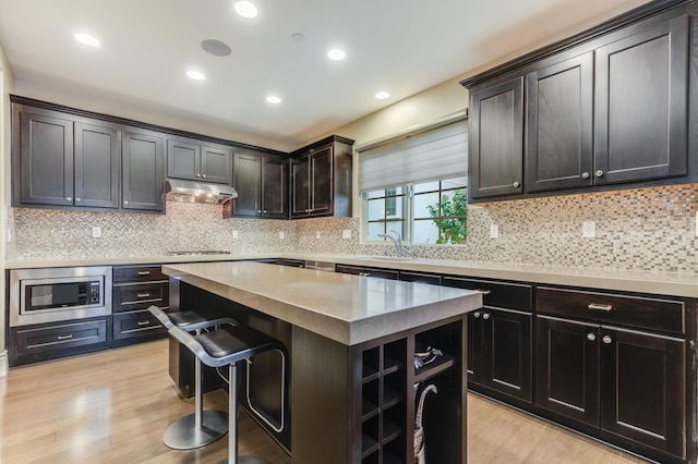 kitchen featuring stainless steel microwave, gas cooktop, light hardwood / wood-style floors, a breakfast bar, and a kitchen island