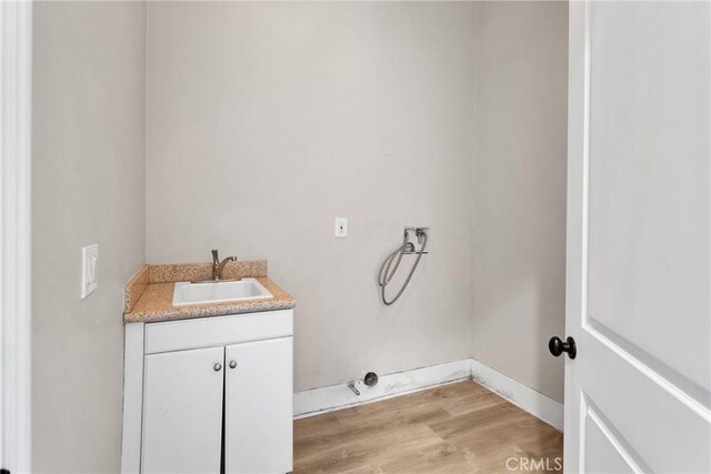 clothes washing area featuring cabinets, sink, washer hookup, and light hardwood / wood-style flooring