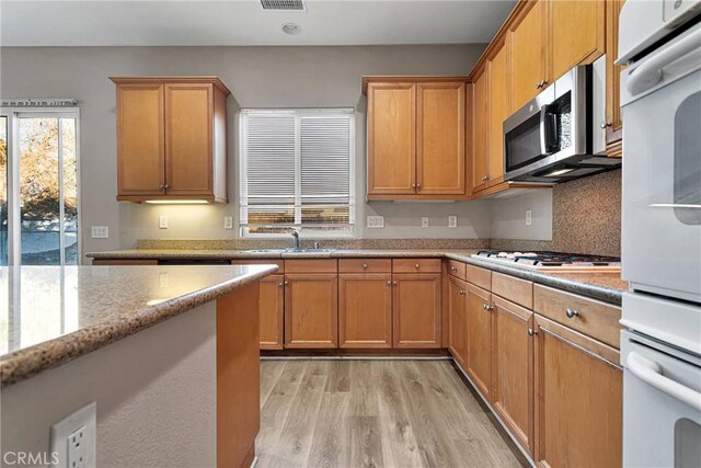 kitchen with white appliances, light hardwood / wood-style floors, light stone counters, and sink