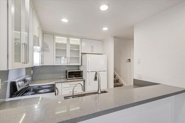 kitchen with stainless steel appliances, dark stone counters, sink, white cabinetry, and range hood