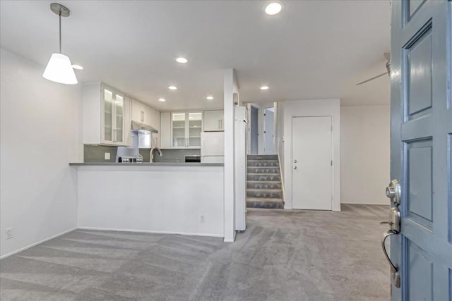 kitchen featuring sink, white cabinetry, white fridge, hanging light fixtures, and light colored carpet