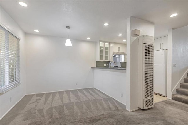 kitchen with light carpet, hanging light fixtures, kitchen peninsula, white refrigerator, and white cabinetry