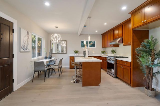 kitchen with a center island, pendant lighting, beamed ceiling, stainless steel range with gas stovetop, and a breakfast bar area