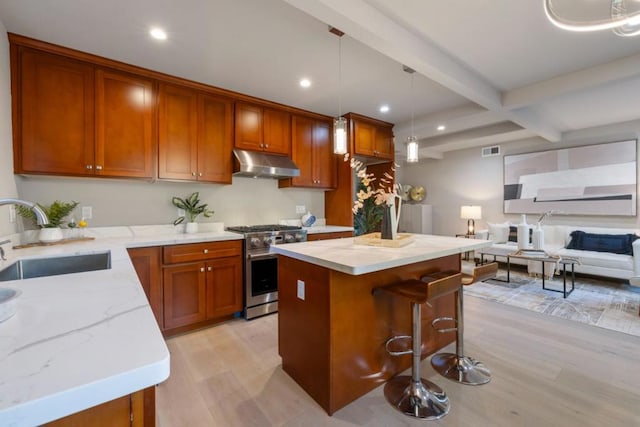 kitchen with high end stove, decorative light fixtures, light wood-type flooring, sink, and beamed ceiling