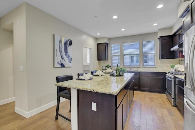 kitchen with a kitchen breakfast bar, light hardwood / wood-style floors, appliances with stainless steel finishes, dark brown cabinets, and a kitchen island