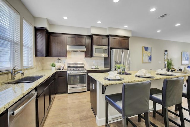 kitchen with a breakfast bar, a center island, sink, appliances with stainless steel finishes, and extractor fan