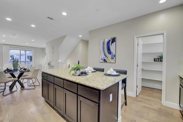 kitchen with dark brown cabinetry, light stone counters, a kitchen island, and light hardwood / wood-style floors