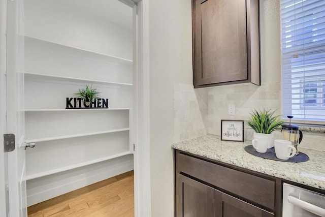 bar with decorative backsplash, light stone countertops, dark brown cabinets, and light wood-type flooring