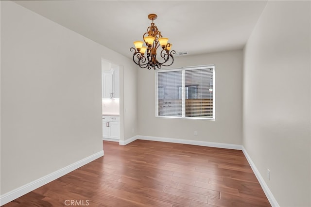 empty room with wood-type flooring and a notable chandelier