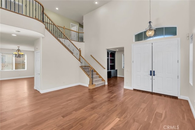 entrance foyer with a towering ceiling, wood-type flooring, and a notable chandelier