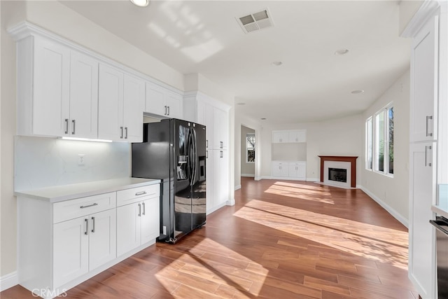 kitchen with black refrigerator with ice dispenser, white cabinetry, hardwood / wood-style flooring, and tasteful backsplash