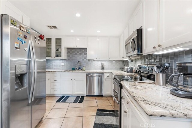 kitchen featuring white cabinetry, sink, backsplash, light tile patterned floors, and appliances with stainless steel finishes