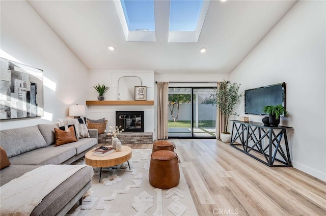 living room featuring light wood-type flooring, lofted ceiling with skylight, and a fireplace